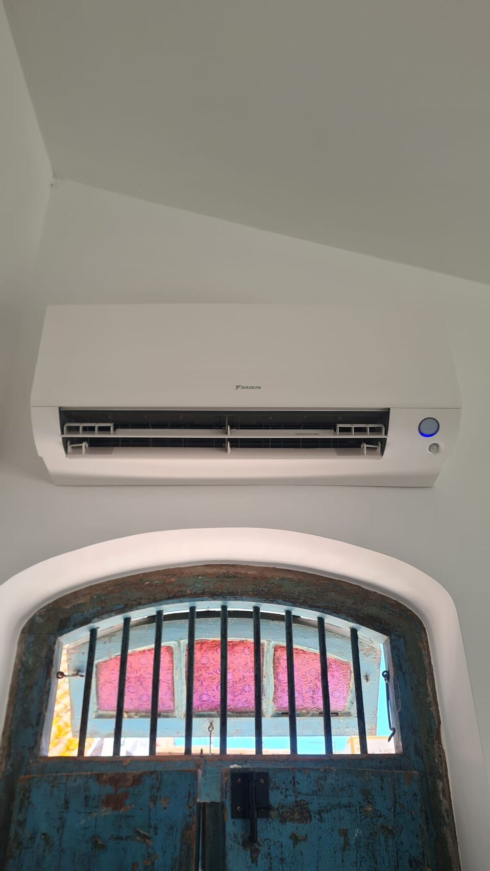 Unidade interior de ar condicionado Daikin instalada sobre janela com grade antiga, Alvor