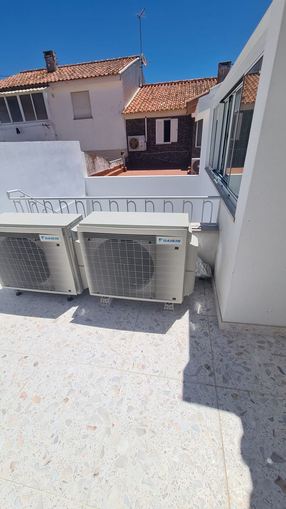 Unidades exteriores de ar condicionado Daikin montadas em telhado com vista para casas típicas, Alvor