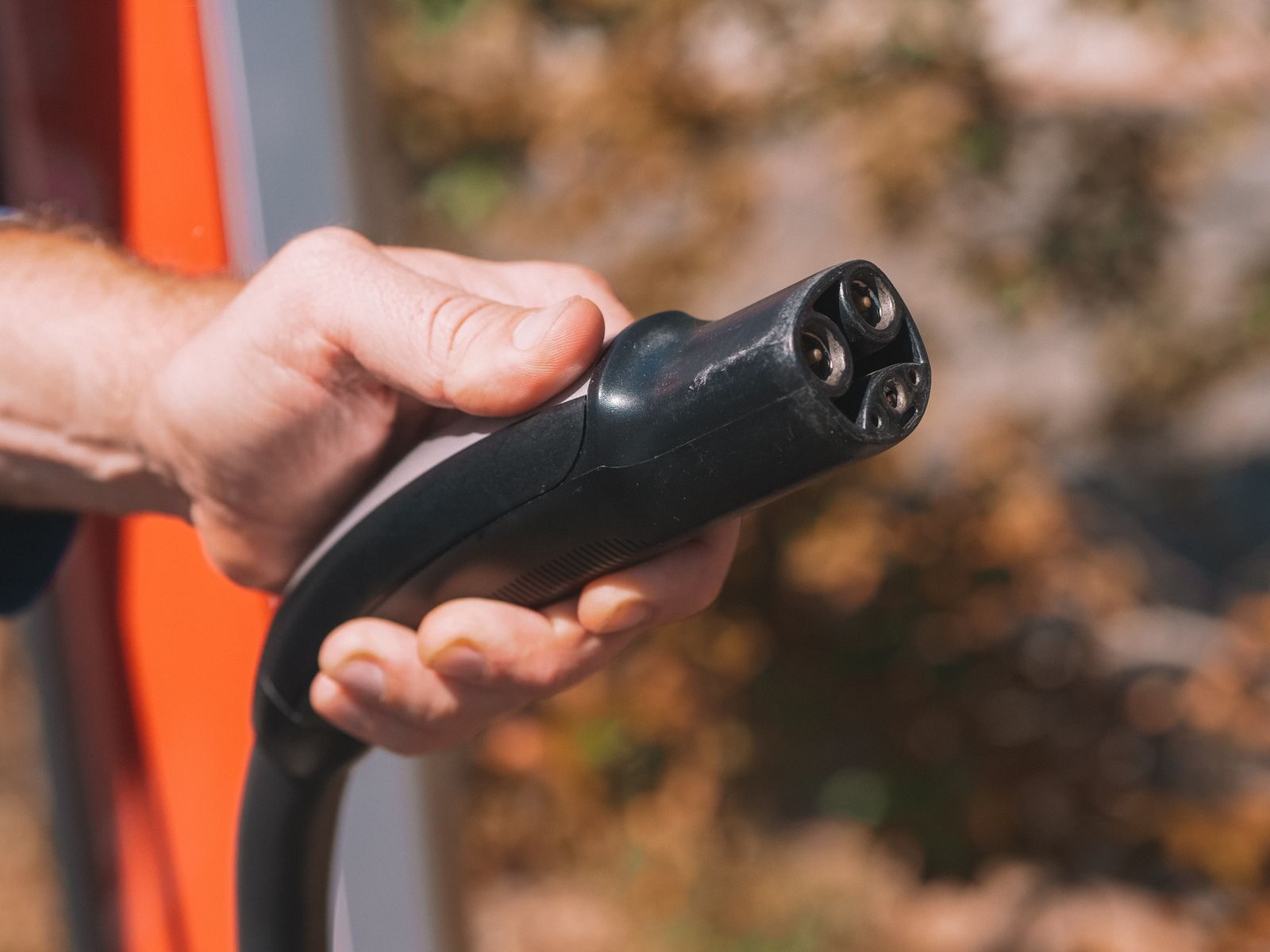 Mão a segurar o conector de um carregador de carro elétrico